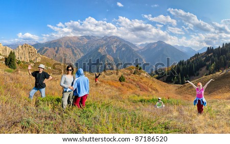 Funny group of people hiking on the meadow of mountain. Aerial view at mountain range and blue sky