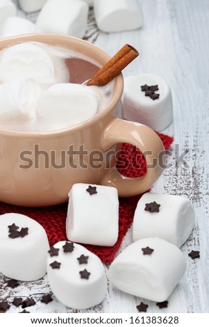 Mug of hot chocolate with marshmallows and cinnamon stick on a white wooden background