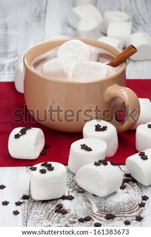 Mug of hot chocolate with marshmallows and cinnamon stick on a white wooden background