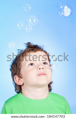 Picture of cute little boy blowing bubbles soap on blue background