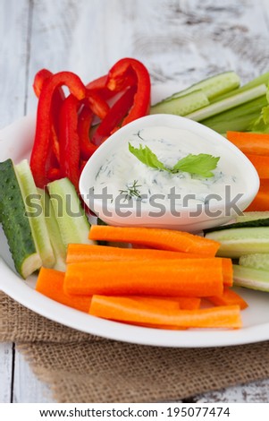 Platter of assorted fresh vegetables with yogurt dip on white wooden background, selective focus