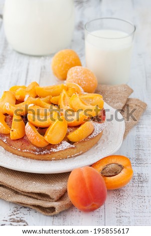 Homemade sweet cake with apricots and glass of milk on white wooden background, selective focus