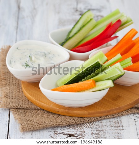 Platter of assorted fresh vegetables with yogurt dip on white wooden background, selective focus