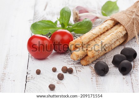 Grissini bread sticks with sesame, olives and basil on white wooden background