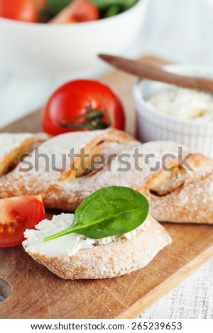 Fresh crispy baguette and cream cheese with herbs on white wooden background, selective focus
