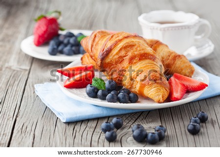 Delicious breakfast with fresh croissants and ripe berries on old wooden background, selective focus