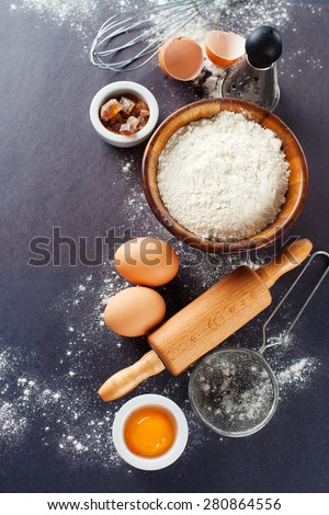 Ingredients and tools for baking - flour, eggs and rolling pin on the black background, top view