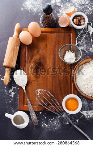 Ingredients and tools for baking - flour, eggs and rolling pin on the black background, top view