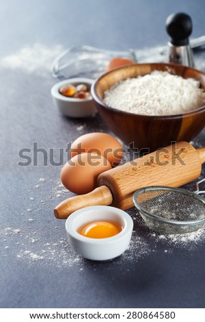 Ingredients and tools for baking - flour, eggs and rolling pin on the black background, selective focus