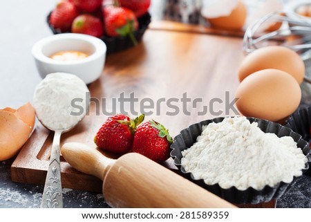 Ingredients and tools for baking - flour, eggs, rolling pin and fresh berries on the black background, selective focus