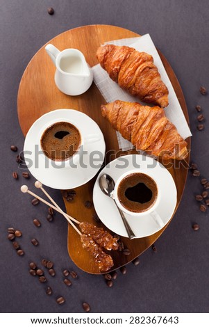 Crispy fresh croissants and cup of coffee espresso on a black background, morning breakfast, selective focus