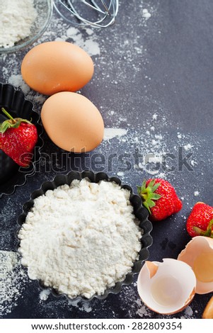 Ingredients and tools for baking - flour, eggs, rolling pin and fresh berries on the black background, top view