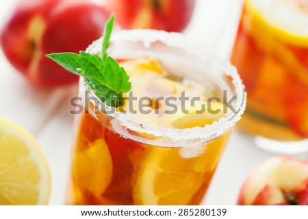 Glass of ice tea with lemon, peach, ice cubes and fresh mint on rustic white wooden background, selective focus