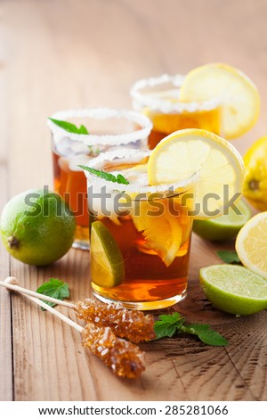 Glass of ice tea with lemon, ice cubes and fresh mint on rustic wooden background, selective focus