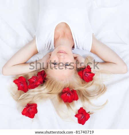 Picture of happy woman with red flowers in blonde hair lying on the white bed