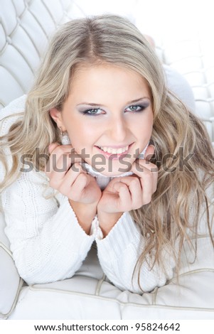 Close-up portrait of a beautiful young blonde woman in white sweater lying on the sofa on white background