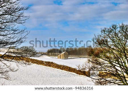 Barn and stone wall lit by winter sunshine in snow covered fields under blue sky