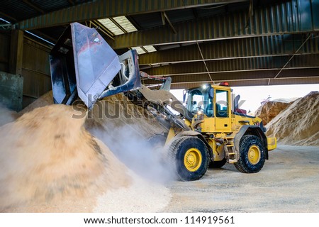 Front loader emptying wood chips in pile for use in pellets manufacturing.