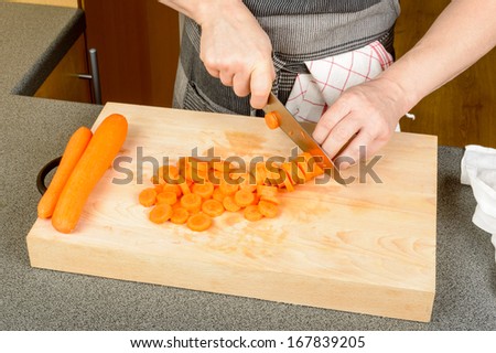 Male hands chopping carrots on wooden cutting board