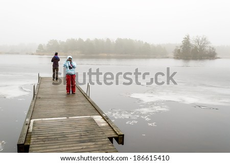 VIRBO, SWEDEN - MARCH 01, 2014: Two females on floating jetty on frozen lake in mist