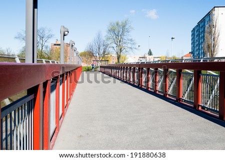 Asphalt walkway bridge with red railings on either side. Perspective slightly from left side.