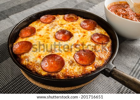 Tasty pan pizza with pepperoni salami and mozzarella in cast iron frying pan.