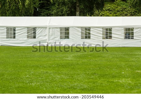Long white party tent at the end of big lawn in park.
