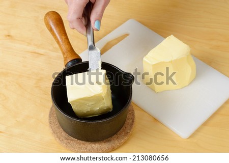 Lump of butter in cast iron pan and on plastic cutting board. Female hand with knife putting butter in pan.