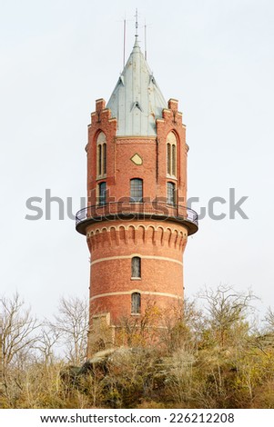 An old historic brick water tower in Ronneby, Sweden. This building was once used to store water for the towns supply. It sits on top of hill with autumn trees below.Overcast sky.