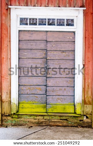 Old weathered door with fine colors and lock. Green line of moss on lower part of door and red paint on surrounding walls. Small windows over door.