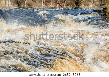 Wild rapids and large volume of water flowing down a river. Riverbank in background.