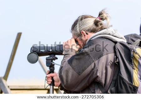 BEJERSHAMN, SWEDEN - APRIL 25, 2015: Unknown birdwatcher using spotting scope to find birds to watch. Person seen from side and behind. Bejershamn is a protected wildlife reserve known for birdlife.