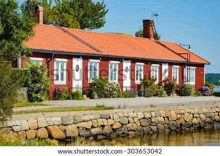 KARLSKRONA, SWEDEN - AUGUST 03, 2015: A lovely red wooden house right by the sea. House has three apartments and fine flowers grow outside. Waters edge in foreground. Ladders on the roof.