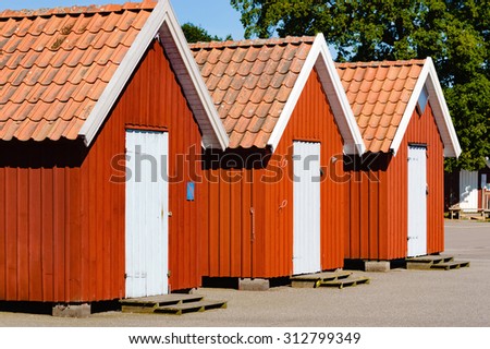 Three lovely red fishing cabins in a row, all with closed white doors. No person visible.