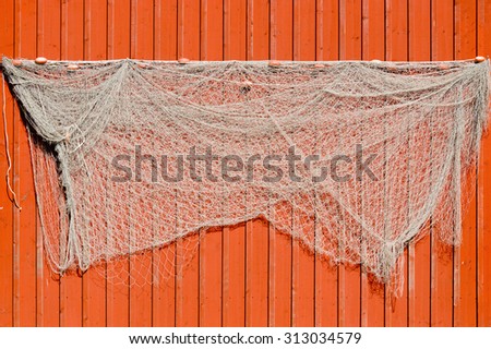 Old fishing nets hanging on red wooden facade of fishing cabins. Nets are sometimes hung on walls like this to dry them out and make cleaning easier. Also its decorative.