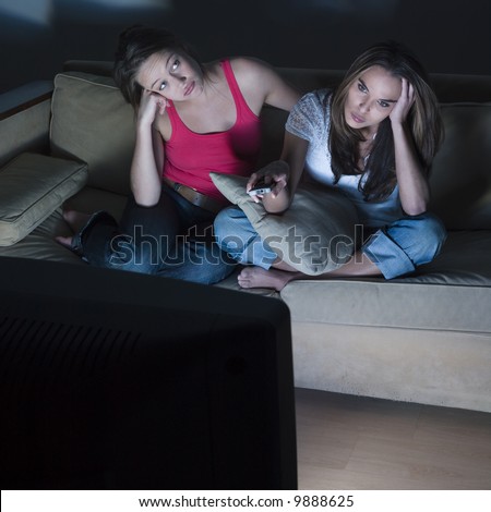 pictures in a living room of two young girls sitting on a couch  geting bored by watching  tv