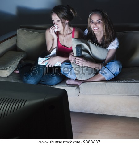 pictures in a living room of two young girls crying sitting on a couch  watching on tv  a sad movie