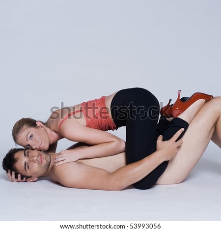 young couple lying down with woman on top and man naked in studio on isolated grey background