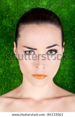 Closeup portrait of a serious beautiful woman raising an eyebrow on green background
