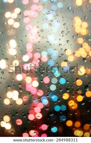 Colorful blur festive lights behind a glass with raindrops on it.