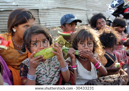 A poor girl in India eating watermelon along with her other family who spend their time begging on the streets. Focus on the eyes of the girl in front.
