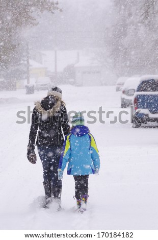 Two girls (perhaps sisters) trudge through a snow-covered neighborhood