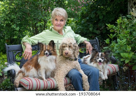 A ninety year-old elderly woman shares a garden bench and companionship with here three dogs.