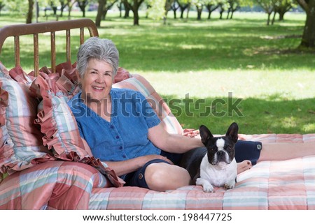 Portrait of a senior woman and her Boston terrier on an old, quilt-covered bed placed in walnut grove as her summer retreat.