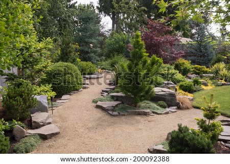 A pebbled path in a large backyard splits, with one fork leading to a lush green lawn, and the other inviting you to explore a meandering path to another area of the yard.