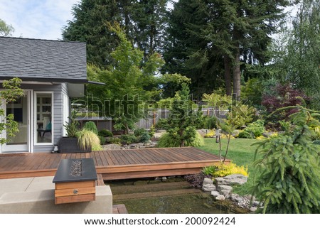 Back yard of a contemporary Pacific Northwest home featuring a deck spanning a creek-like water feature with a landscaped lawn in the background.