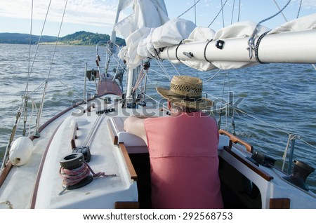 A senior man relaxes on board his classic ketch sailboat as he contemplates the distant shore.