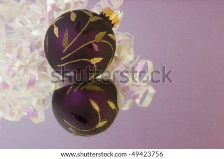 purple Christmas bauble with gold leaves and pearl white metallic ribbon on a soft purple background