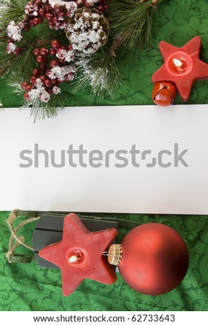 red Christmas star candles with icy fir branch, green sled, ornament on soft green background with copyspace