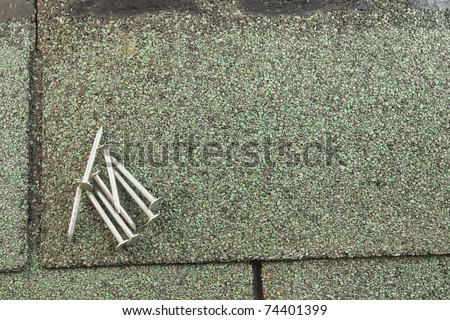 several roofing nails on a green asphalt shingle